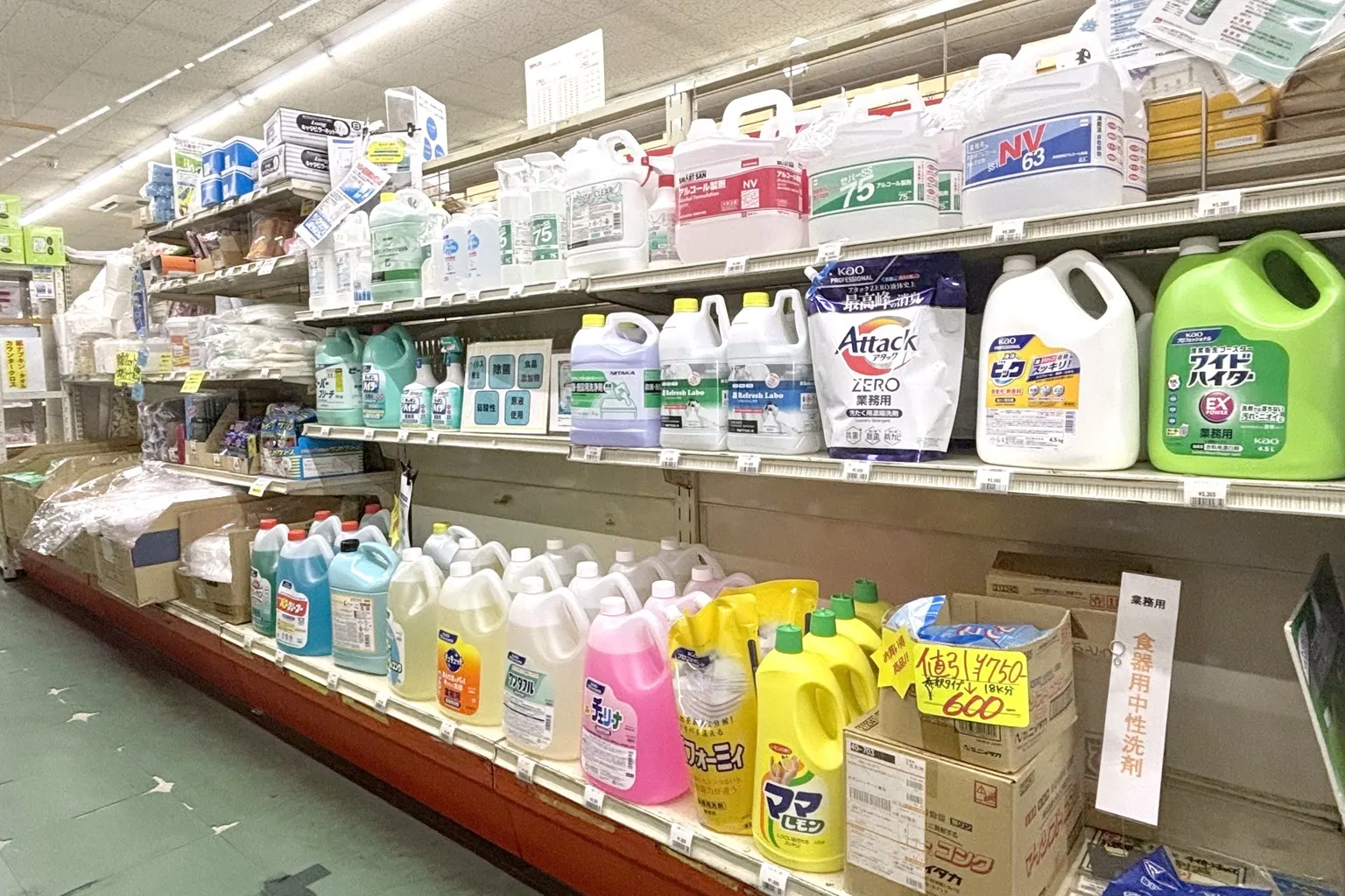 業務用の洗剤・アルコール製剤・漂白剤の大きなボトルが、値札や値引きの札とともに並ぶ店内の棚